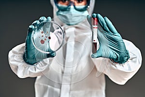 Unrecognizable female scientist with bacteriological protection suit examining a petri dish in the laboratory