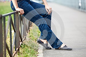 Unrecognizable female sitting on steel fence of pedestrian pathway, blue jeans and comfortable shoes