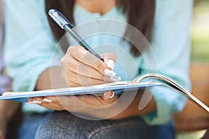 Unrecognizable female student sitting outdoors, making notes, closeup