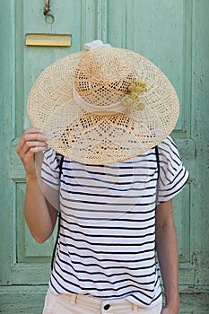 Unrecognizable female tourist woman wearing big straw standing in front of vinatage turquoise wooden door at old