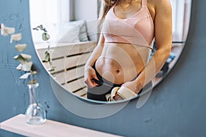 Unrecognizable fit woman with perfect abdominal muscles and obliques in front of mirror look at her reflection