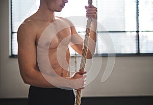 Fit young man in gym standing topless , holding climbing rope.