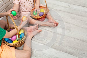 Unrecognizable girl and boy sitting on the floor with colorful Easter eggs in two wicker baskets