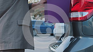 Unrecognizable girl business woman customer driver in gray stylish jacket walks down street carries holds in hand purple