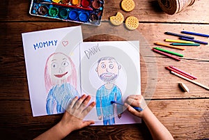 Unrecognizable girl drawing pictures of her mother and father