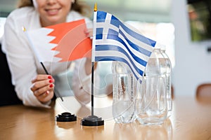 Unrecognizable girl sets midget flags of Greece and Bahrein before international negotiations photo