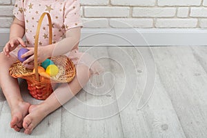 Unrecognizable girl sitting on the floor with colorful Easter eggs in wicker basket at home