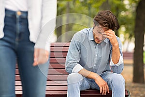 Unrecognizable Girlfriend Leaving Sad Boyfriend Sitting On Bench In Park