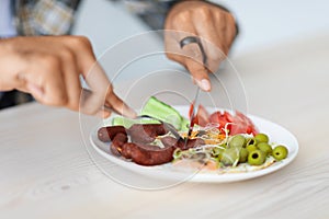 Unrecognizable guy cutting fresh vegetables and sausages, closeup photo