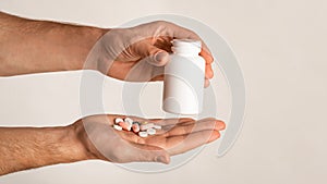 Unrecognizable guy holding bottle of meds and different pills on light background, space for design. Panorama