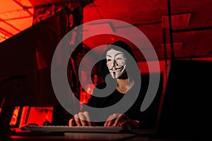 Unrecognizable hacker man wearing anonymous mask and sweatshirt typing on wireless keyboard breaking password using