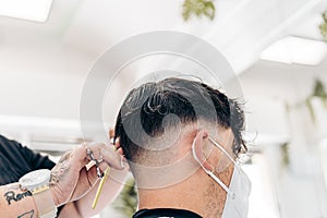 Unrecognizable hairdresser cutting the hair of a boy with mask in a salon