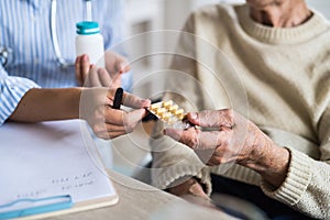 An unrecognizable health visitor explaining a senior woman in wheelchair how to take pills.