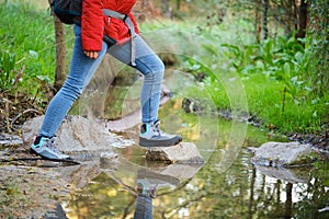 Unrecognizable hiker legs crossing a creek in a forest.