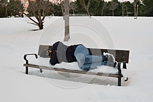 Unrecognizable homeless man sleeping on bench in snowy cold winter