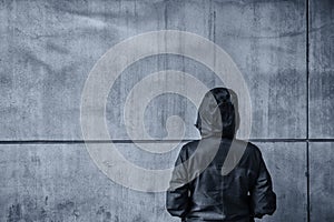 Unrecognizable hooded female person facing concrete wall as insu