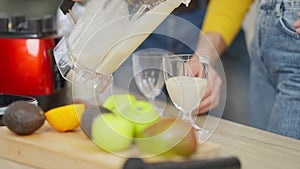 Unrecognizable husband pouring milkshake in glasses as woman waiting for healthful drink. Happy couple having healthy