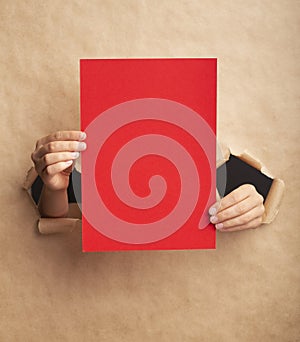 Unrecognizable lady holding red sheet with empty space through ripped craft paper