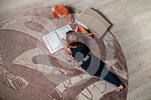 Unrecognizable little girl in a dark blue dress reading book lying on the floor near teddy bear. Child reads story for toy. Top v