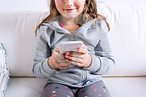 Unrecognizable little girl sitting on sofa, playing with smartph