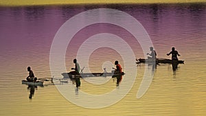 Unrecognizable local fishermen fishing in small wooden boats at colorful sunrise