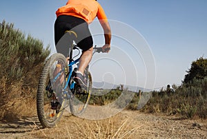 Unrecognizable male cyclists from behind pedaling down a dirt road in nature. Mountain biking