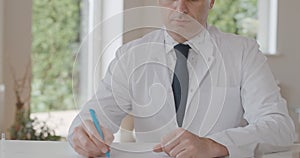 Unrecognizable male doctor sitting at the table with documents. Confident Caucasian physician posing in his office in