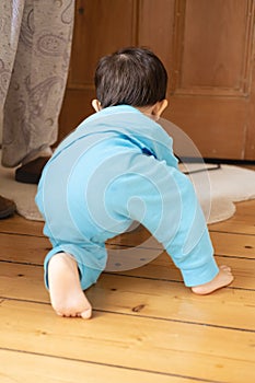 An unrecognizable male multiracial Malaysian and Spanish baby wearing blue pajamas crawling and walking way on wooden floor