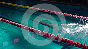Unrecognizable male swimmer jumps off starting block and start swims in pool. Professional athlete training: dive and