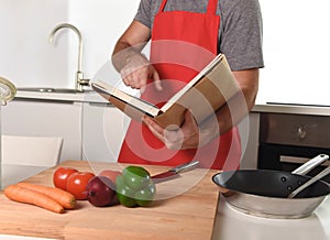 Unrecognizable man in apron at kitchen following recipe book healthy cooking