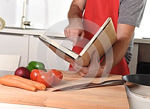 Unrecognizable man in apron at kitchen following recipe book healthy cooking