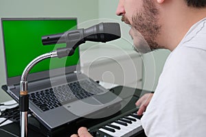 Unrecognizable man blogger, youtuber, influencer recording a video playing the electronic piano and singing at home
