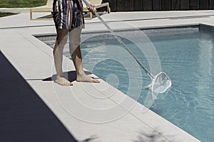 Unrecognizable man cleaning the swimming pool manually with white cleaning net at his house