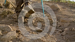 Unrecognizable man climbing mountain with trekking poles