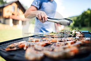 Unrecognizable man cooking seafood on a barbecue grill in the backyard.