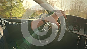 An unrecognizable man is driving a car. In the shot, hands are on the steering wheel of a premium car, the summer sun