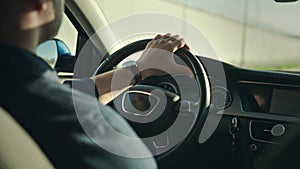 An unrecognizable man is driving his car. The shot shows hands on the steering wheel, the dashboard and the street.