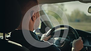 An unrecognizable man is driving his car. The shot shows hands on the steering wheel, the dashboard and the street.