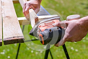 Unrecognizable man in the garden sanding wooden planks. DIY home improvement, restoration, carpentry concept.