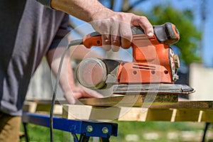 Unrecognizable man in the garden sanding wooden planks. DIY home improvement, restoration, carpentry concept.