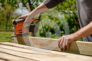 Unrecognizable man in the garden sanding wooden planks. DIY home improvement, restoration, carpentry concept.