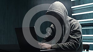 Unrecognizable man hacker wearing sweatshirt with hood typing on laptop and breaking password.