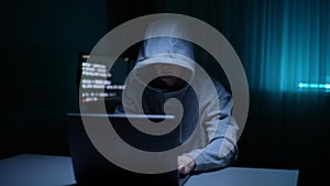 Unrecognizable man hacker wearing sweatshirt with hood typing on laptop computer keyboard and breaking password in dark