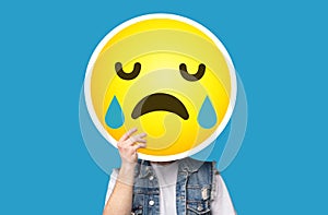 Unrecognizable man hiding his face behind crying sad emoticon emoji