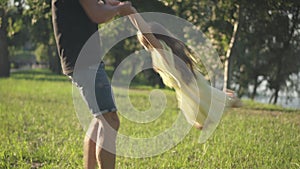 Unrecognizable man holding hands of girl spinning child in sunshine in summer spring park. Cheerful Caucasian father