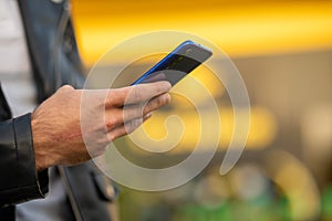 Unrecognizable man holding mobile phone in hand, blurred yellow background