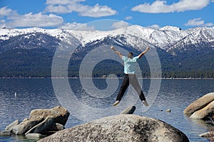 Unrecognizable man jumps off boulder with outstretched arms while at Lake Tahoe.