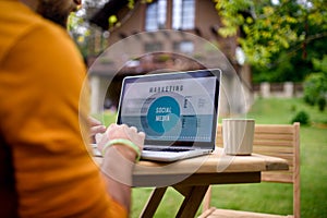 Unrecognizable man with laptop working outdoors in garden, home office concept.
