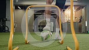 Unrecognizable man male footballer soccer player sportsman legs hit ball through arches jump over barriers training in