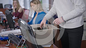 Unrecognizable man packing cardboard box in office with blurred women working at background. Unknown male Caucasian